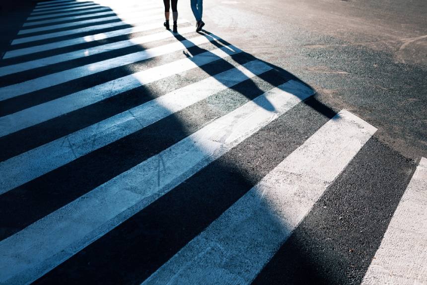 Figures crossing crosswalk zebra crossing in distance shadows on road daylight