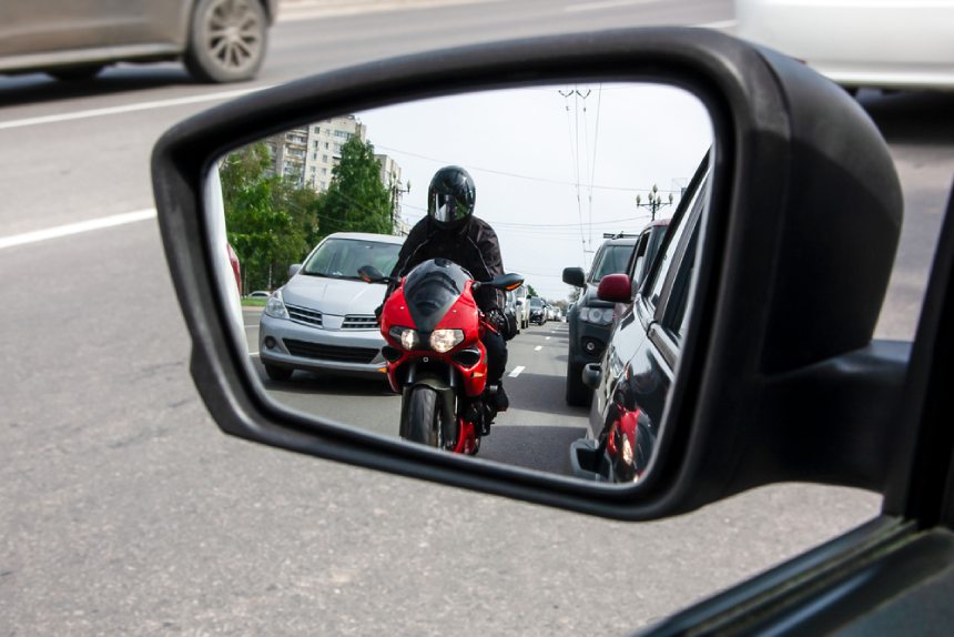 Mirando por el espejo retrovisor motocicleta que se aproxima carril dividiendo entre el tráfico ocupado