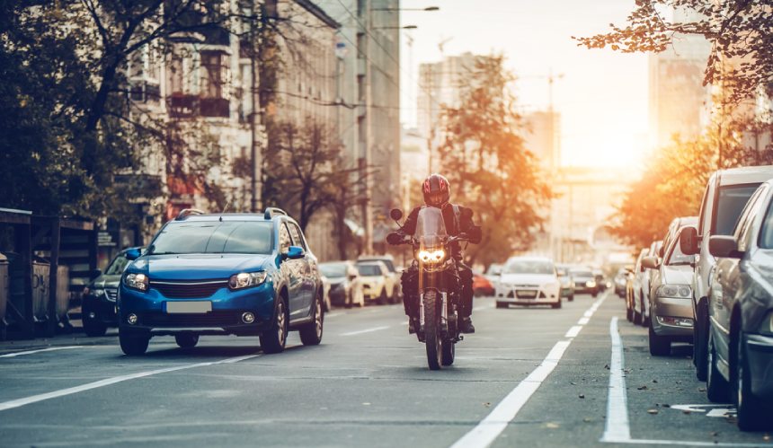 Motorcyclist riding alongside blue car in urban traffic in daytime