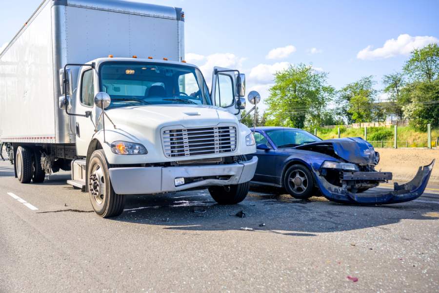 A white semi truck and a blue car shortly after a bad accident