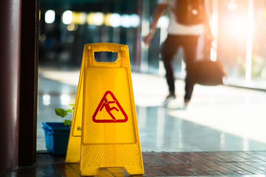 Yellow slip and fall warning sign with person walking in background carrying a backpack