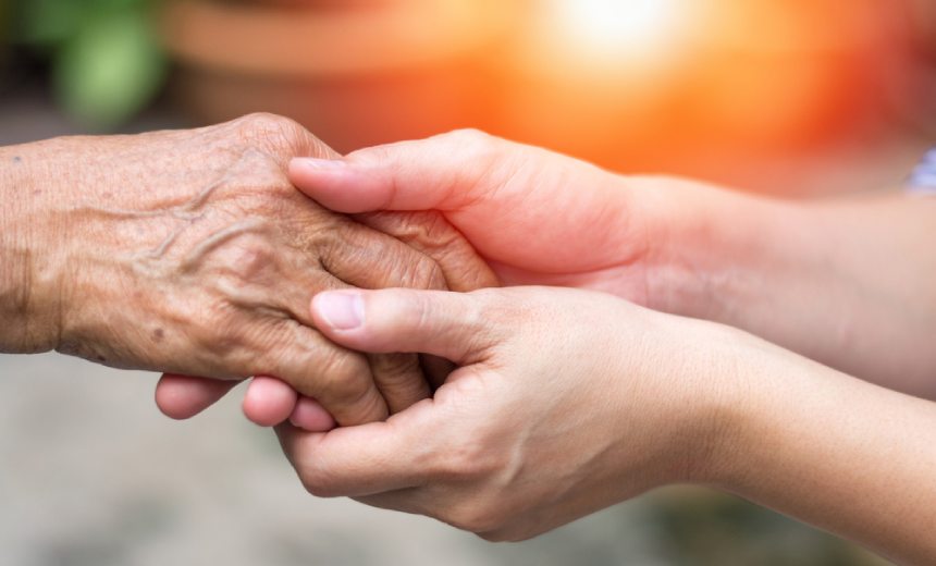 Young caregiver holding elder persons hand in care setting