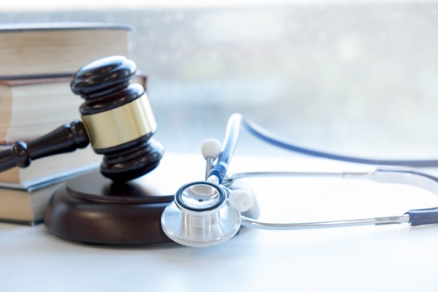 Gavel and stethoscope on white table with legal textbooks in background.