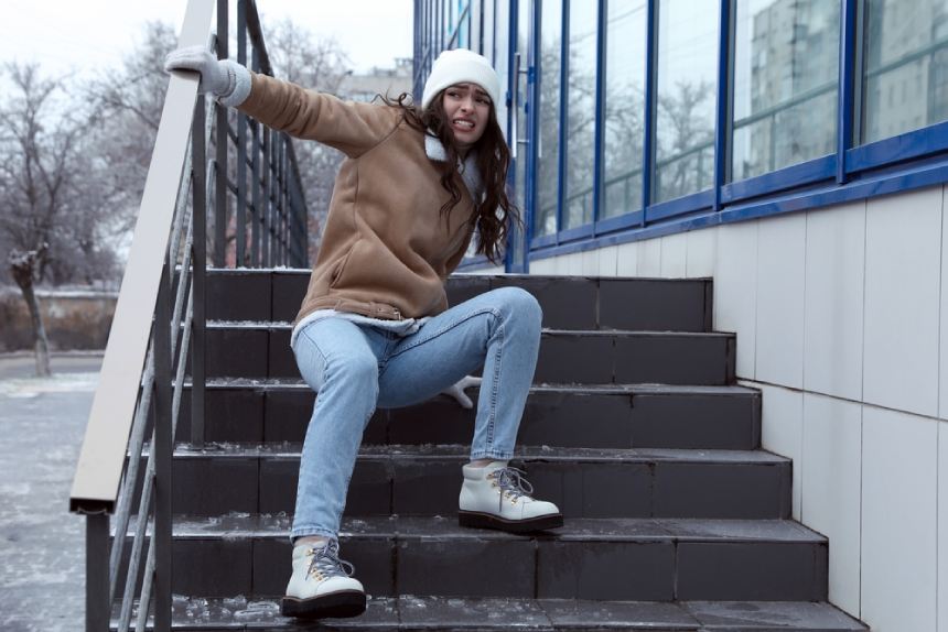 Young woman in pain sitting on stairs holding onto railing after falling on ice