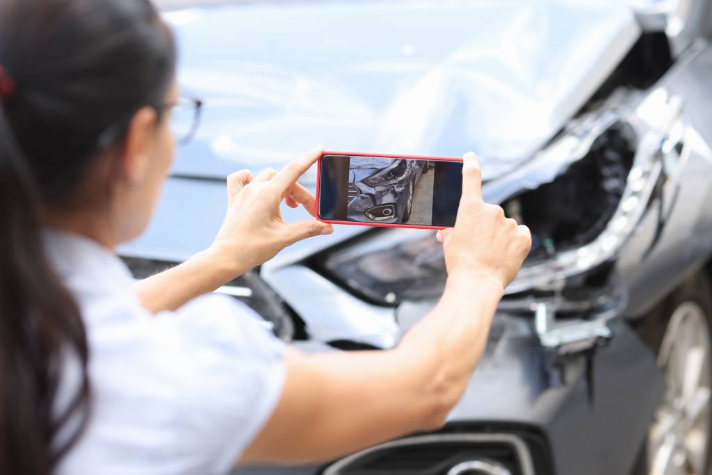 Female insurance agent taking picture of car damage on cellphone after car crash