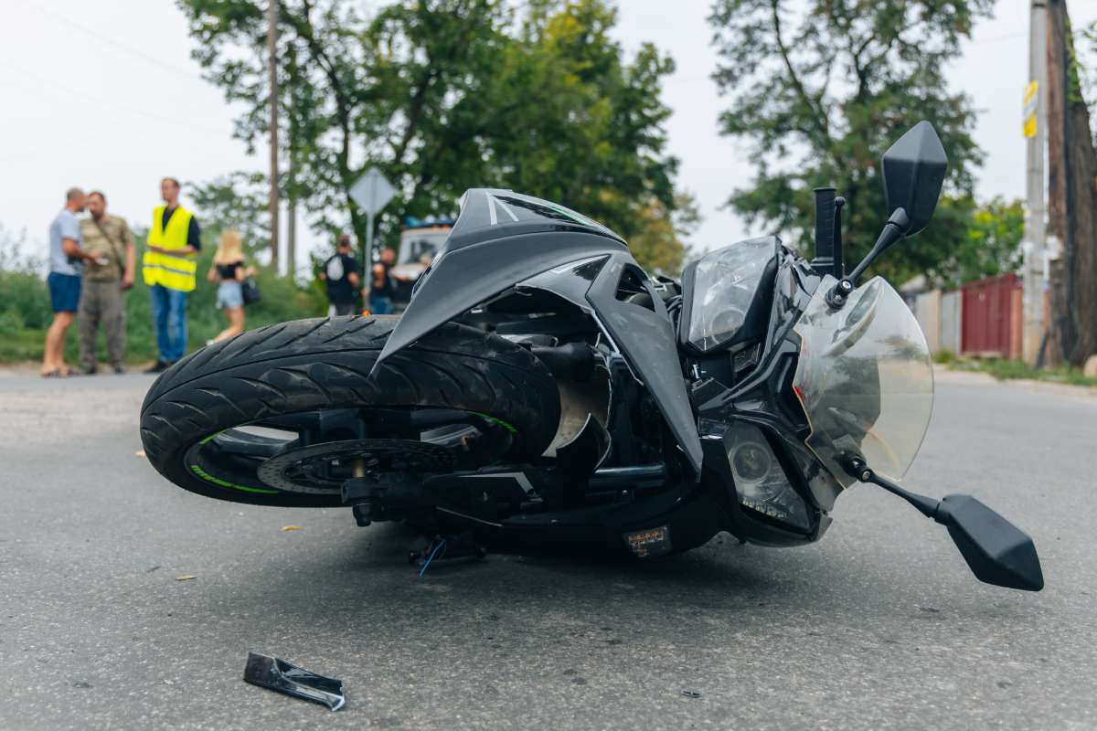 Close up of a motorcycle lying on road after crash with drivers involved in background