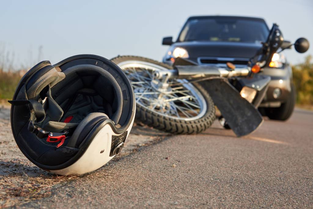 Casco de motocicleta y motocicleta en la carretera con el coche en el fondo después de la colisión