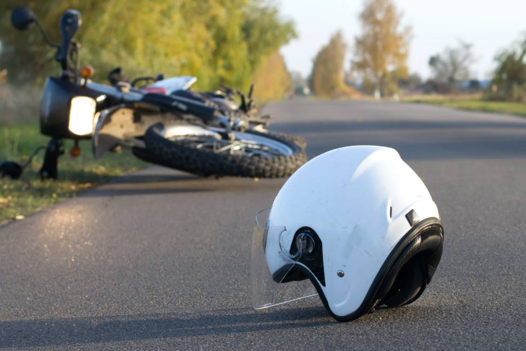 Casco de motociclista blanco y motocicleta desechada al fondo tras un accidente