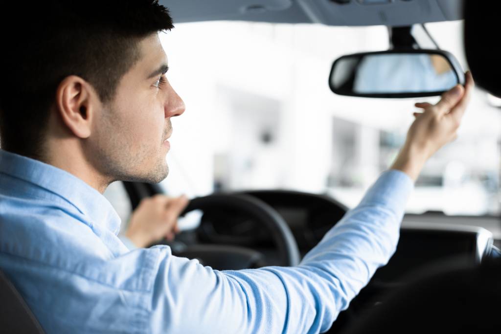 Un hombre mira por el retrovisor, dando ejemplo de hábitos de conducción seguros.