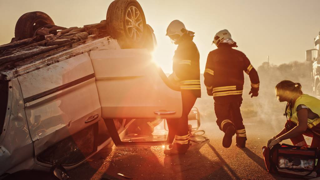 Dos bomberos y un paramédico inspeccionan un vehículo volcado en un accidente con vuelco, intentando determinar si se puede extraer a algún ocupante del siniestro y atenderlo.