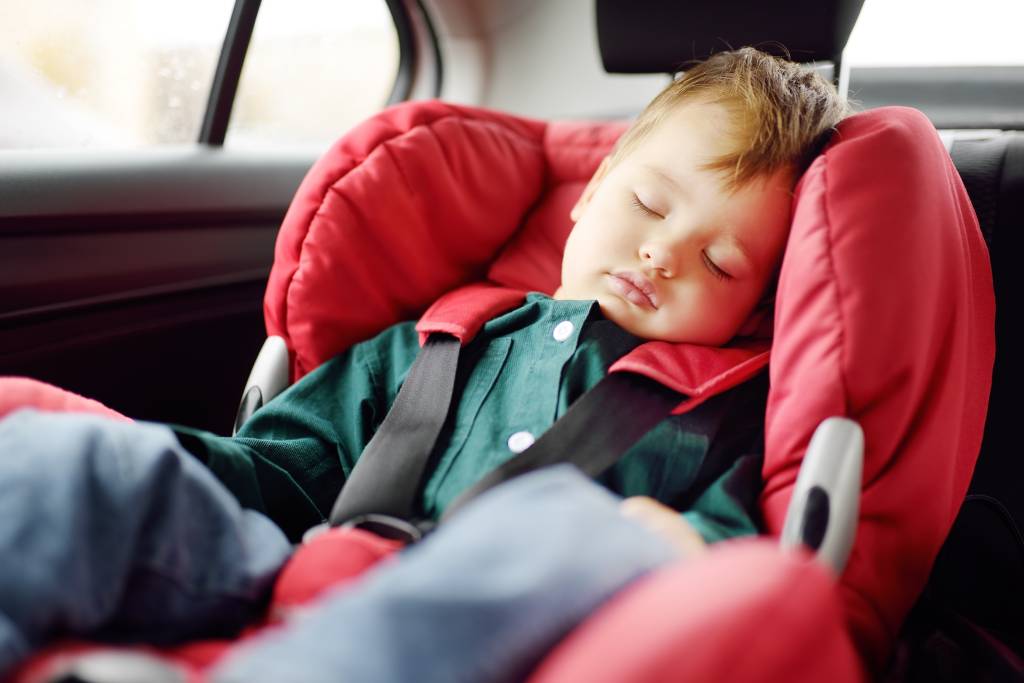 A baby boy sleeping in a car seat.