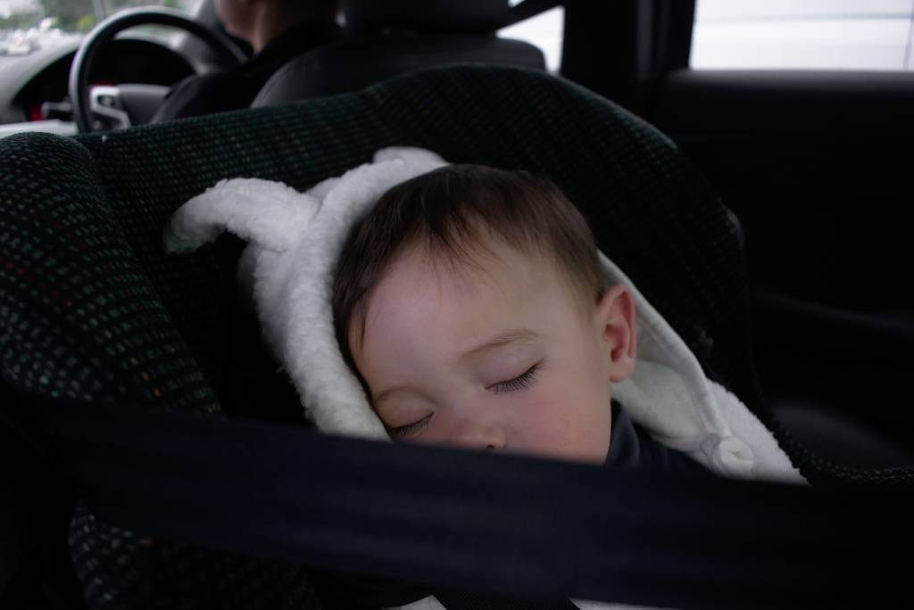 A baby bundled up and sleeping in a rear-facing car seat.