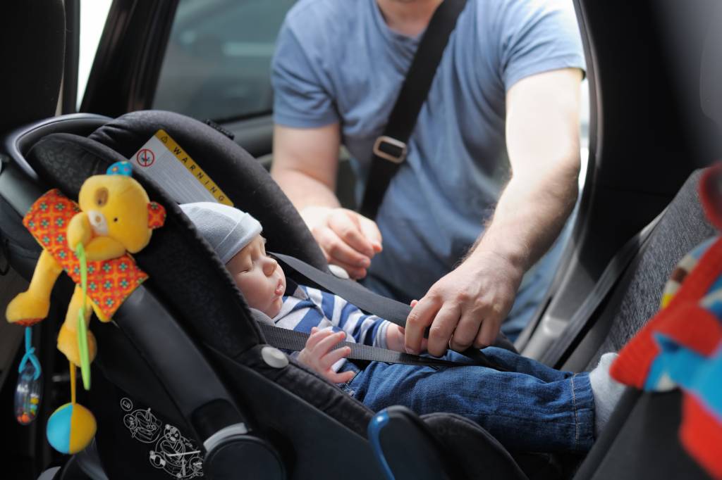 Un padre colocando a un bebé en una silla de coche.