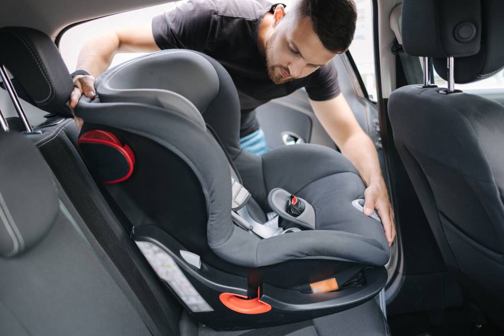 A man installs a forward-facing car seat into the back seat of his vehicle.