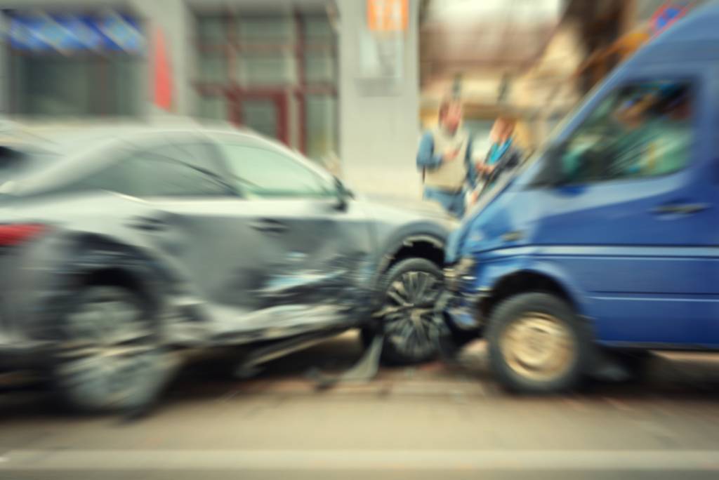 A somewhat blurred image of a gray sedan and a blue transit van colliding at a diagonal.