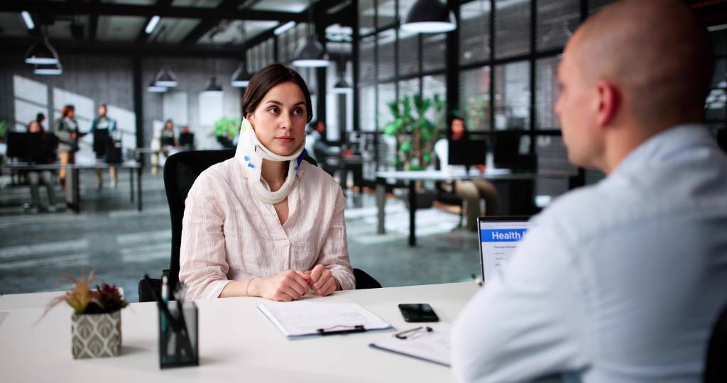 A woman in a neck brace sits across from a personal injury lawyer as he discusses her case options.